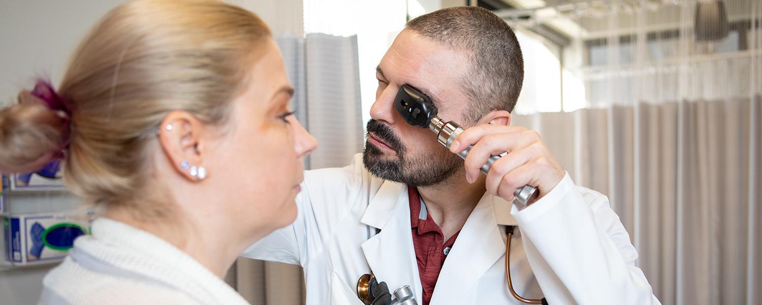 A male nursing graduate students examines a patient's eyes.